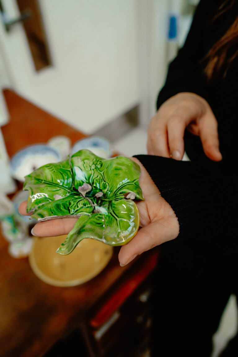 A candle holder made from ceramics. It is formed in the shape of a large broad leaf and painted a glossy green.