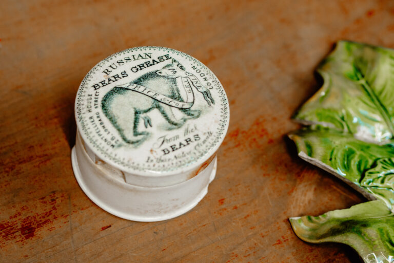 An old white pottle with a painting of a bear on its lid. The pottle has various manufacturer marks on it and is labelled "Russian Bears Grease (from the bears in their native climate)".